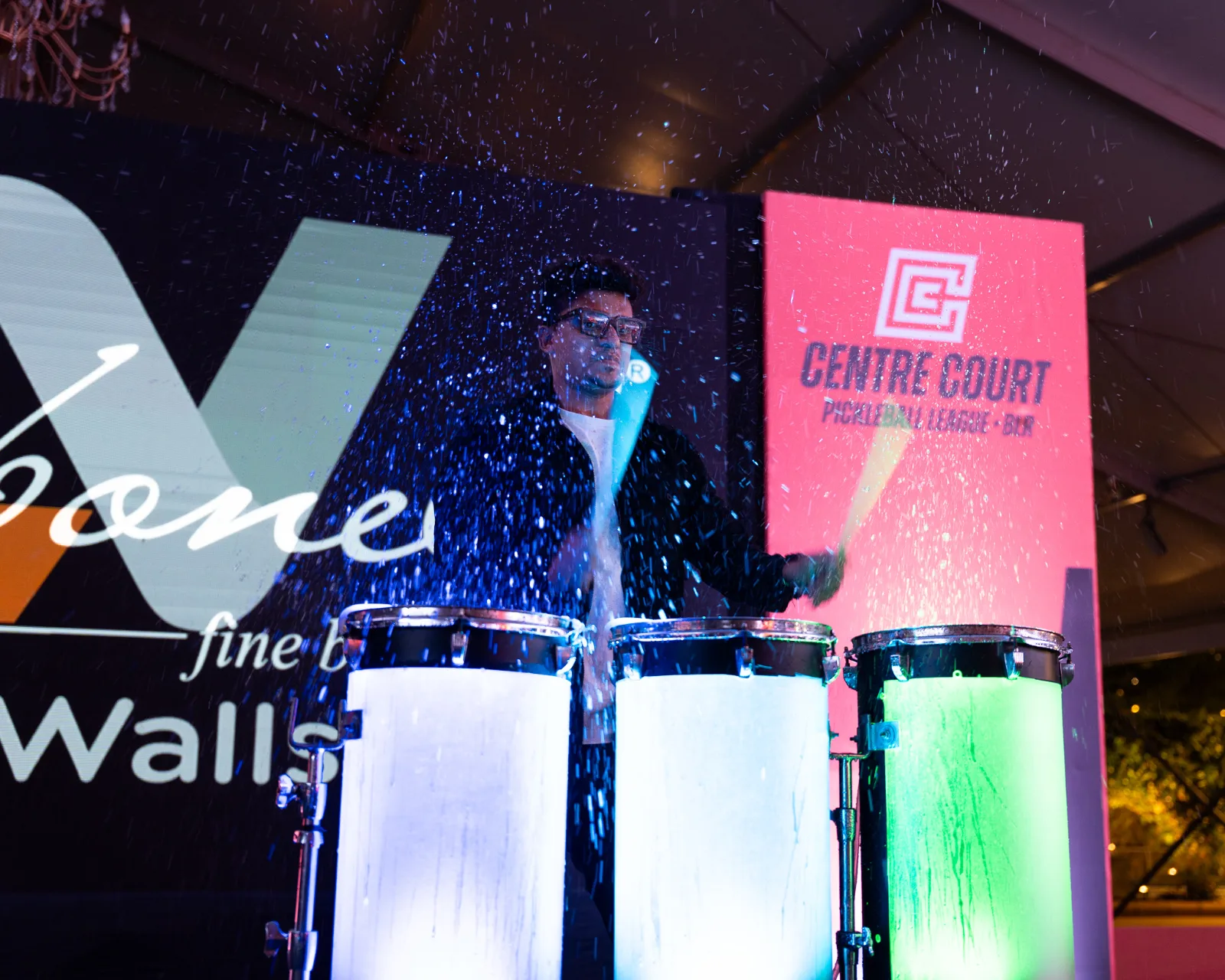 A percussionist plays lit drums on a stage beside a Centre Court Pickleball League banner