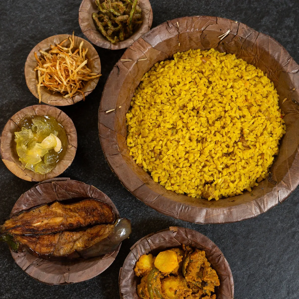 A Bengali meal served in leaf bowls: rice, fried aubergine, crisp potato and a curry